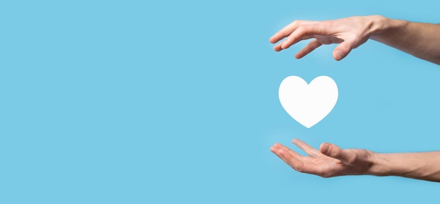 Männliche Hand, die Herz, wie Symbol auf blauem Hintergrund hält. Freundlichkeit, Nächstenliebe, reine Liebe und Mitgefühl Konzept. Banner mit Kopienraum