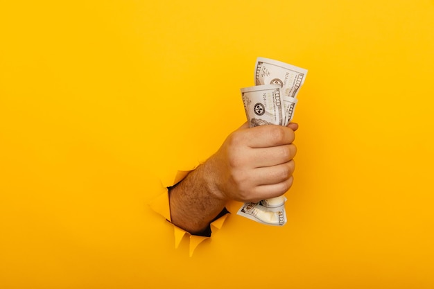 Foto männliche hand, die zerknitterte dollarbanknoten durch loch im gelben hintergrund hält