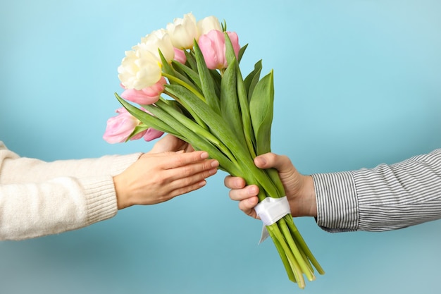 Männliche Hand gibt Tulpenstrauß zur weiblichen Hand auf blauem Hintergrund