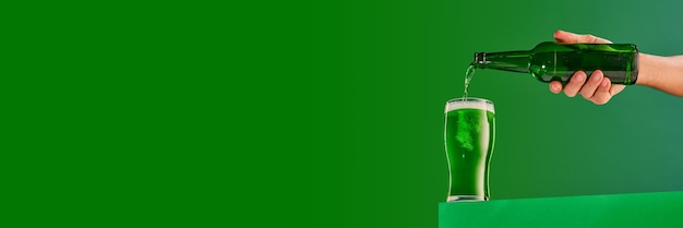 Männliche Hand gießt grünes, schaumiges, frostiges Bier in Glas über grünem Hintergrundkonzept von St. Patricks