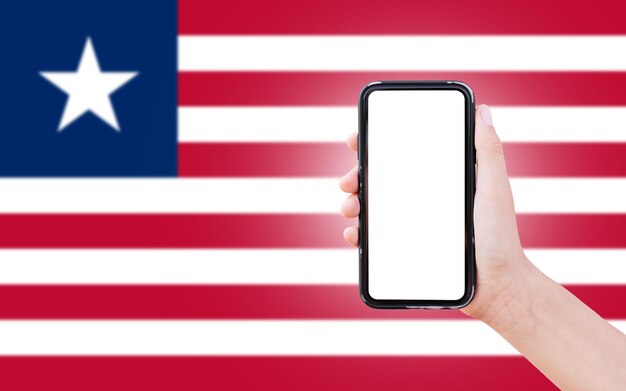 Männliche Hand hält Smartphone mit leerem Bildschirm auf dem Hintergrund der unscharfen Flagge Liberias Nahaufnahme