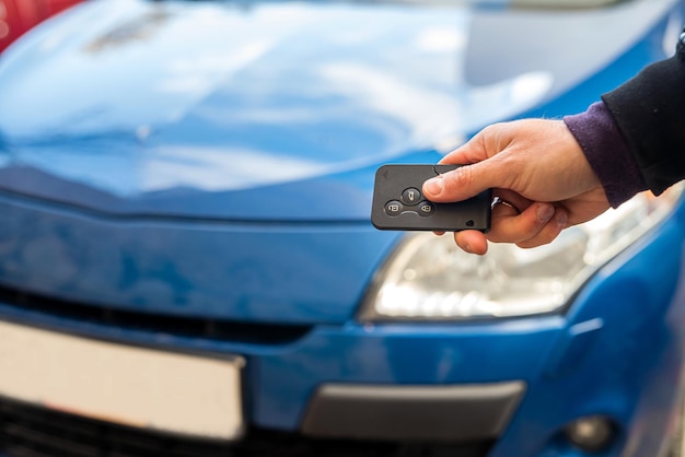 Männliche Hand in einem Business-Anzug hält schwarze Autoschlüssel auf einem Hintergrund eines blauen schönen eigenen Autos. Geschäftskonzept. Das Konzept des Autokaufs. Luxuskonzept