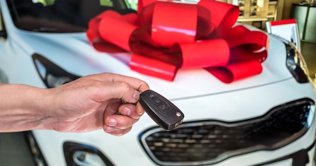 Männliche Hand mit Autoschlüsseln mit Auto auf Hintergrund. Mieten oder kaufen