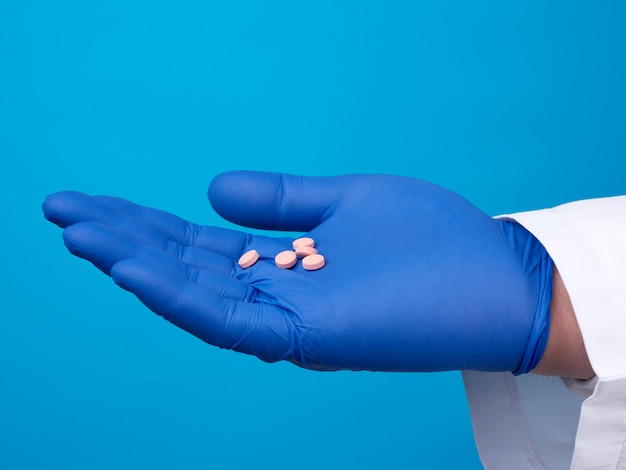 Männliche Hand mit blauen sterilen Handschuhen hält runde rosa Pillen