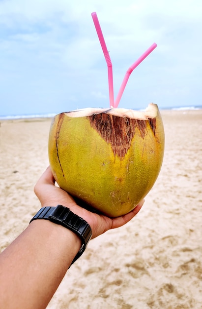 Männliche Hand mit einer Kokosnuss am Strand