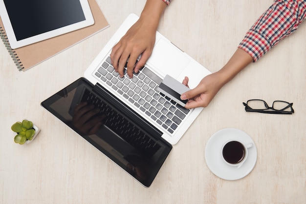 Männliche Hand mit Laptop mit Kredit, der online am Schreibtisch bezahlt