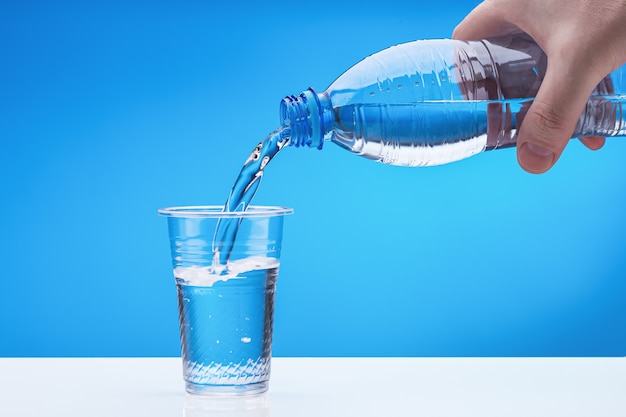 Männliche Hand mit Plastikflasche. Wasser fließt in Glas. Speicherplatz kopieren.