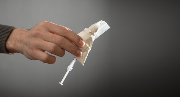 Männliche Hand zeigt Spritze und Plastikpackung Heroin