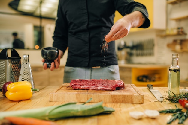 Männliche Person, die rohes Fleisch auf Holzbrett mariniert