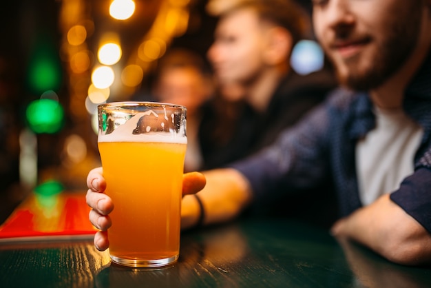 Männliche Person hält Glas mit Bier an der Bartheke in einer Sportkneipe, Fußballfan