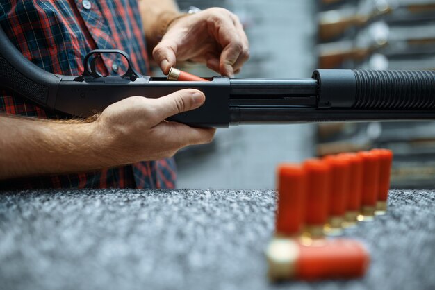 Männliche Person mit Gewehr lädt Munition am Schaufenster im Waffenladen.