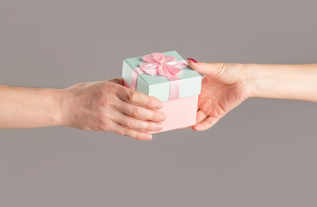 Männliche und weibliche Hände, die rosa Geschenkbox halten. Mädchen gibt dem Mann ein Geschenk. Frauenhände, die Geschenk halten Geschenkbox in der Hand, Überraschungs- und Urlaubskonzept. Mannhände, die valentinstaggeschenk halten.
