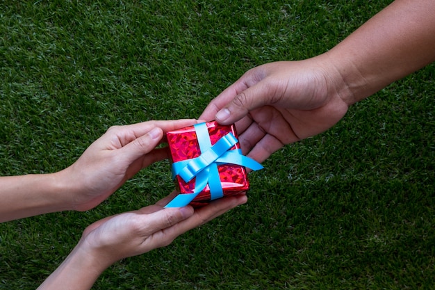 Männliche und weibliche Hände mit roter Geschenkbox mit Bogen