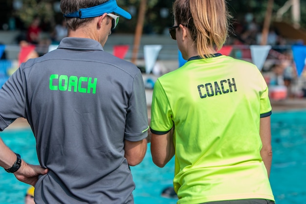 Männliche und weibliche Schwimmtrainer, die an einem Swimmingpool im Freien zusammenarbeiten