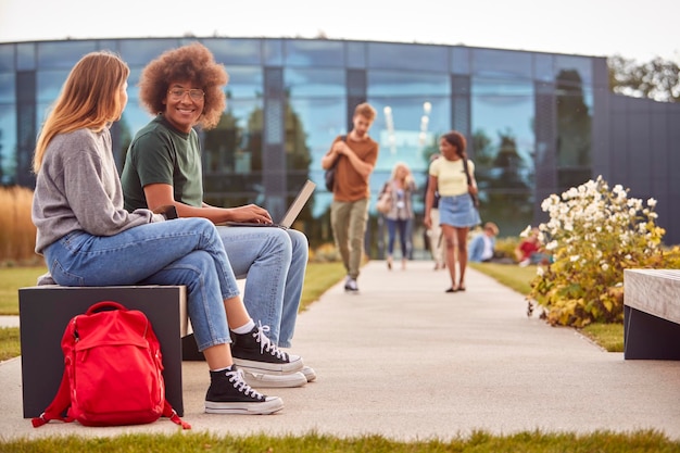 Männliche und weibliche Universitäts- oder College-Studenten, die draußen auf dem Campus sitzen und gemeinsam am Laptop arbeiten