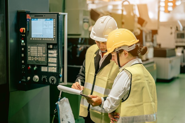 Männliche und weibliche Wirtschaftsingenieure in Schutzhelmen diskutieren neue Projekte, während sie Blaupausen in der industriellen Fertigungsfabrik verwendenIngenieur- und Architektenkonzept