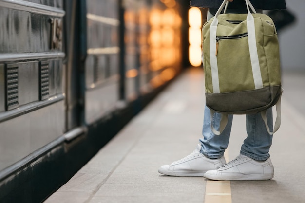 männliche wartende u-bahn auf plattform gutaussehender mann in weißen turnschuhen und jeans mit rucksack