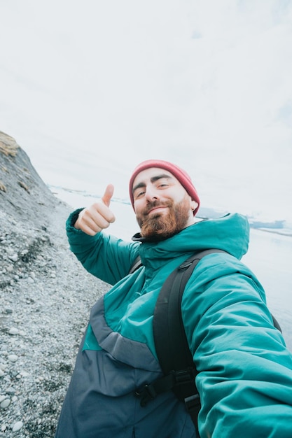 Männlicher Alleinreisender auf Island glücklich über Roadtrip neue Erfahrungen Freiheit leben und Rucksackreisen erkunden Bärtiger Hipster, gutaussehender Typ, der das gute Zeichen für die Kamera macht und beim Wandern ein Selfie macht