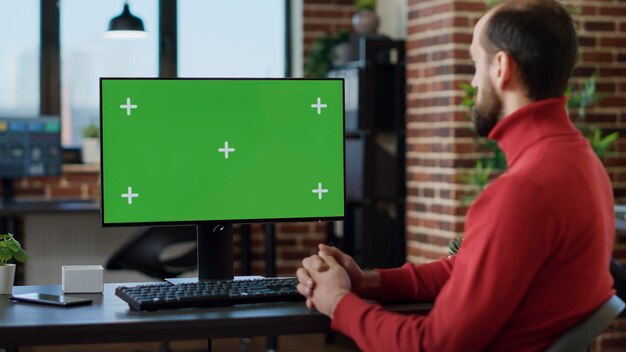 Foto männlicher angestellter arbeitet mit grünem bildschirm auf dem monitor und nutzt technologie am schreibtisch. büroangestellter analysiert