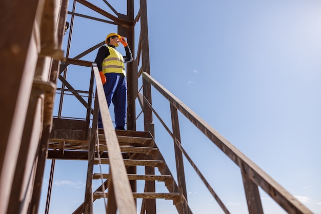 Männlicher Arbeiter, der auf der Treppe unter blauem Himmel steht