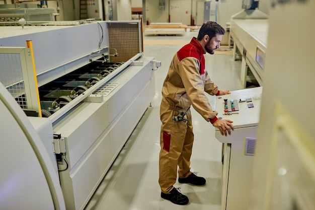 Männlicher Arbeiter, der eine automatisierte Maschine verwendet, während er in einer Holzbearbeitungsfabrik arbeitet