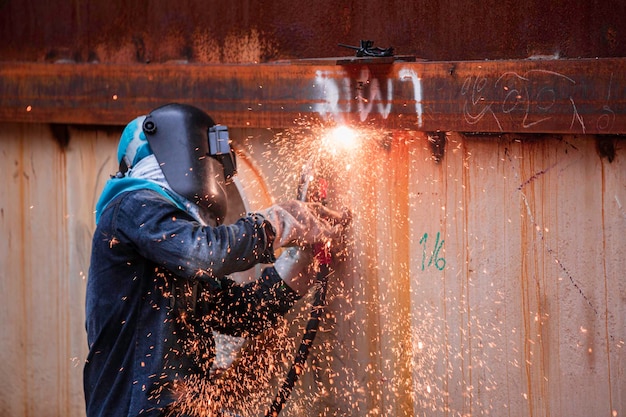 Männlicher Arbeiter, der Schutzkleidung trägt und Reparaturschweißfunkenschalen für Industriebauöl und -gas oder Lagertanks in geschlossenen Räumen repariert.