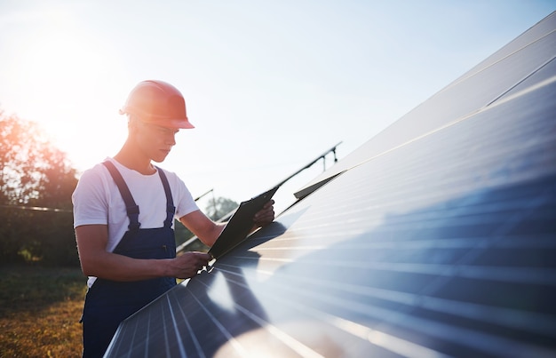 Männlicher Arbeiter in blauer Uniform im Freien mit Solarbatterien am sonnigen Tag.