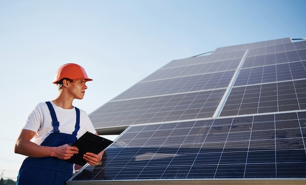 Männlicher Arbeiter in blauer Uniform im Freien mit Solarbatterien am sonnigen Tag.