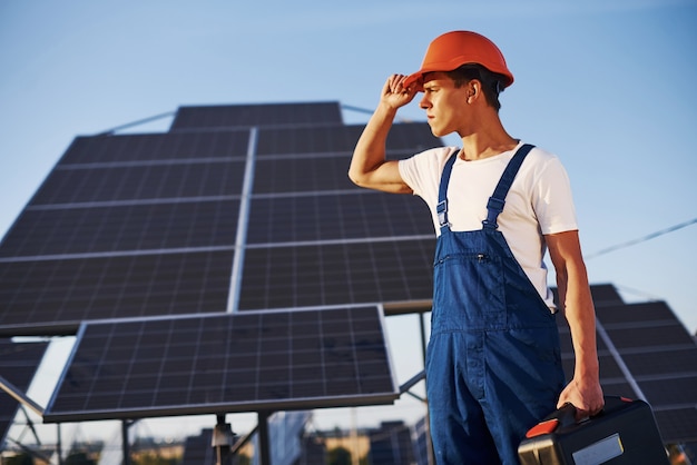 Männlicher Arbeiter in blauer Uniform im Freien mit Solarbatterien am sonnigen Tag.