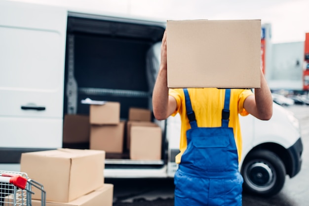 Männlicher Arbeiter in Uniform hält Karton in Händen, Verteilungsgeschäft. Frachtlieferung. Leerer, klarer Behälter