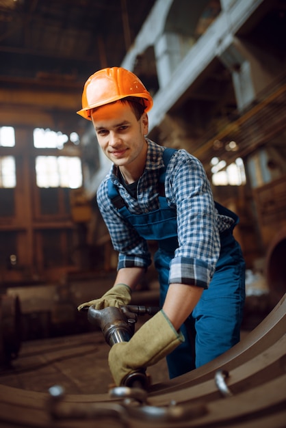 Männlicher arbeiter in uniform und helm entfernt ab werk schuppen von metallwerkstücken. metallverarbeitende industrie, industrielle herstellung von stahlprodukten