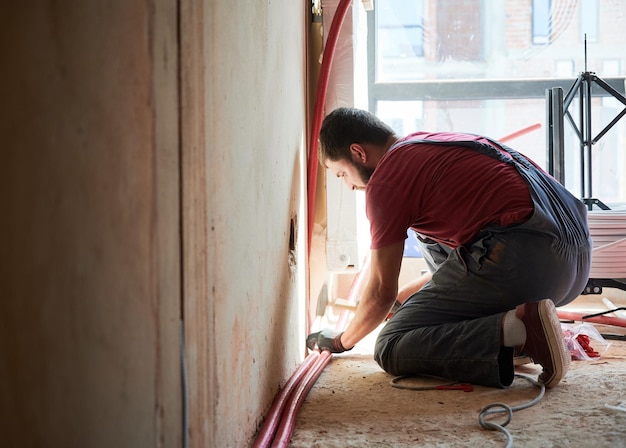Männlicher Arbeiter installiert Heizkörper in einem neuen leeren Raum neben dem Fenster