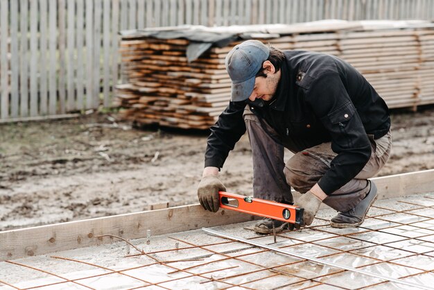 Männlicher Arbeiter misst das Konstruktionsniveau der Bewehrung für das Fundament eines im Bau befindlichen Hauses