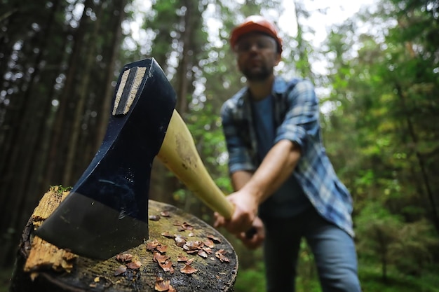 Männlicher Arbeiter mit einer Axt, die einen Baum im Wald hackt.