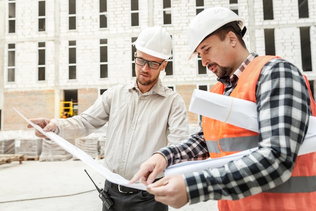 Männlicher Architekt und Entwickler mit Bauplänen, die Architektenprojekte auf der Baustelle diskutieren