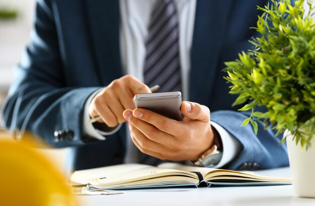 Männlicher Arm im Anzug hält Telefon und silbernen Stift