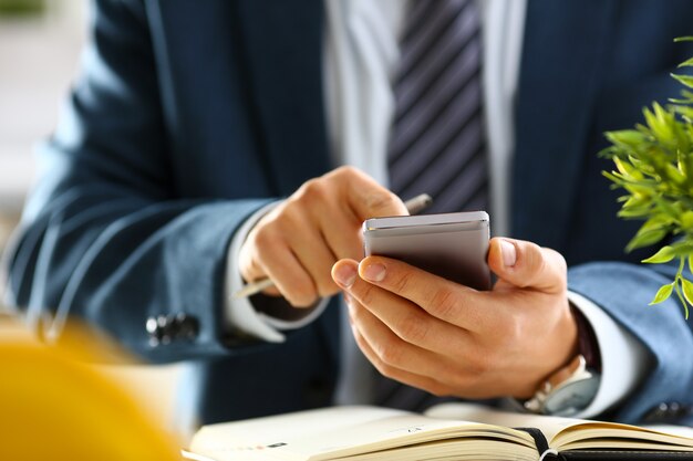 Männlicher Arm im Anzug hält Telefon und silbernen Stift