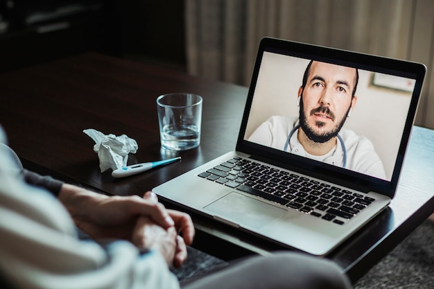 Männlicher Arzt auf dem Laptop-Bildschirm während eines Videoanrufs mit einem Patienten mit Coronavirus-Symptomen