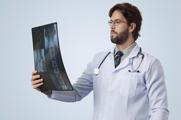 Männlicher Arzt auf einem grauen Hintergrund, der eine Röntgenaufnahme betrachtet.