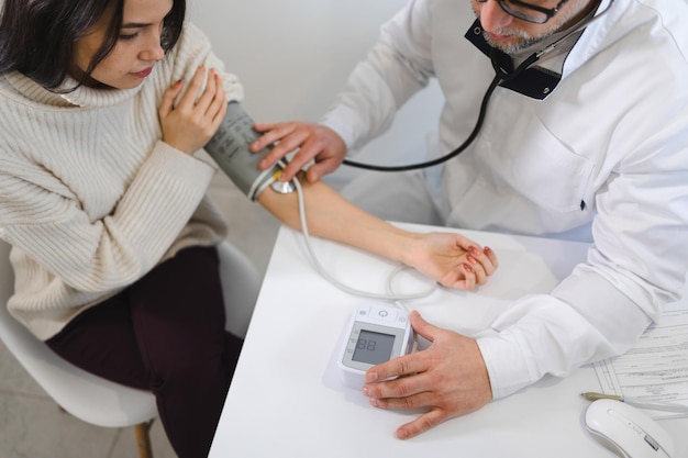 Männlicher Arzt bei der ärztlichen Untersuchung misst den Blutdruck einer Patientin. Frau auf Termin beim Kardiologen