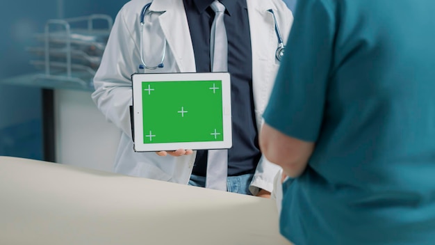 Männlicher Arzt, der bei der Untersuchung mit dem Patienten einen horizontalen grünen Bildschirm auf einem digitalen Tablet hält. Arzt zeigt isolierten Kopierraum mit Mockup-Vorlage, leerem Hintergrund und Chroma-Key auf dem Display.