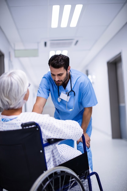 Männlicher Arzt, der mit dem älteren Patienten im Rollstuhl interagiert