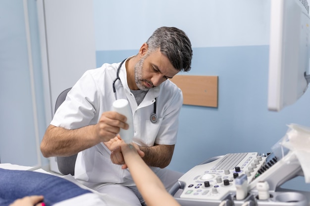 Männlicher Arzt, der Ultraschalluntersuchung der Armvenen des Patienten in seinem Büro tut Junge Frau, die Ultraschalluntersuchung in der Klinik übergibt Arztarbeit Medizinische Forschung