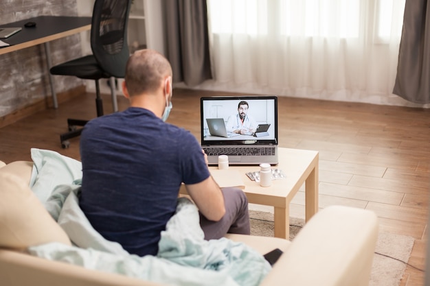 Männlicher Arzt, der während der Quarantäne mit dem Patienten in einer Videokonferenz spricht.