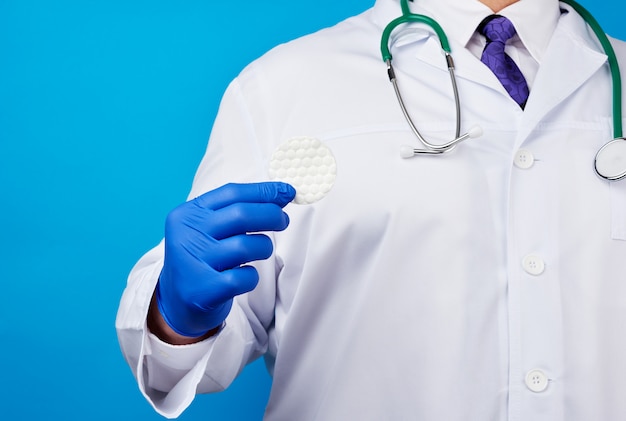 Männlicher Arzt in einem weißen Kittel, blaue Latex-medizinische Handschuhe, die eine Baumwollkosmetikscheibe halten