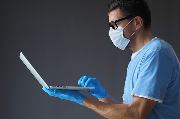 Männlicher Arzt in medizinischer Maske und Handschuhen arbeitet im Laptop.