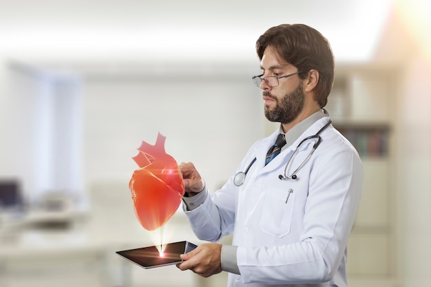 Männlicher Arzt in seinem Büro, der ein virtuelles Herz betrachtet, das aus einer Tablette kommt