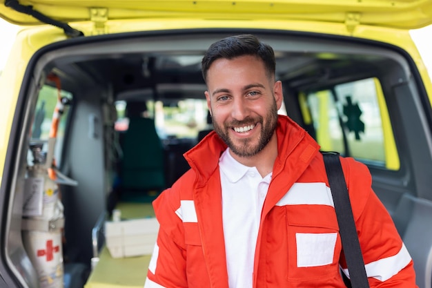 Männlicher Arzt lächelt in die Kamera-Krankenwagen-Crew, die auf dem Hintergrund verschwommen arbeitet