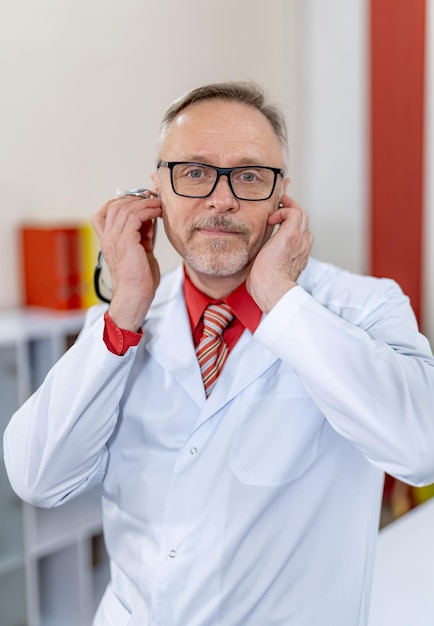 Männlicher Arzt legte Stethoskop an seine Ohren. Lustige Emotionen in der Klinik. Rotes Hemd und weißes Peeling. Nahansicht.