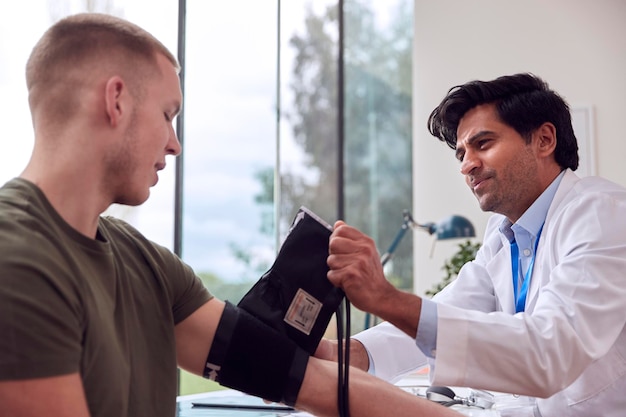 Männlicher Arzt oder Allgemeinmediziner untersucht jungen männlichen Patienten, der den Blutdruck mit einem Blutdruckmessgerät nimmt